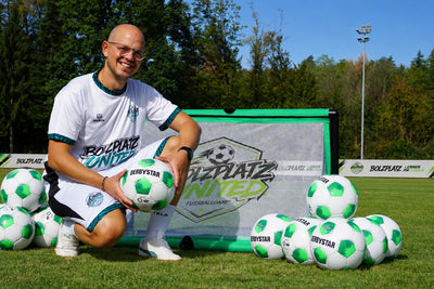 Trainer kniet mit einem Ball vor dem Bolzplatz United Minitor